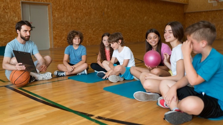 students sitting on gym floor with teacher and basketball
