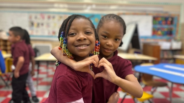 2 elementary students hugging, making heart sign