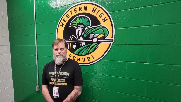 Teacher Sterling Harris in front of school logo